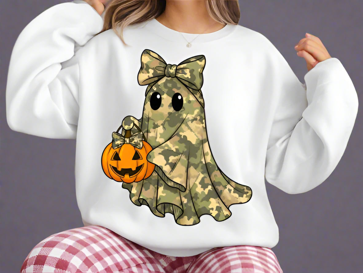 White sweatshirt with a camo ghost holding a pumpkin design, worn by a person sitting in front of a Christmas tree.
